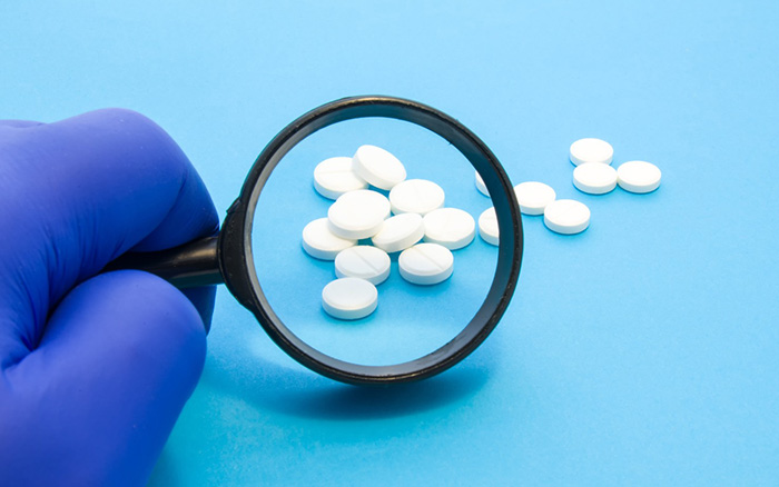 Gloved hand with magnifying glass on pills