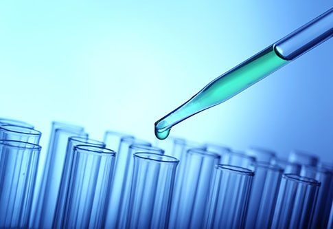 Closeup of a pipette dropping green sample into a test tube